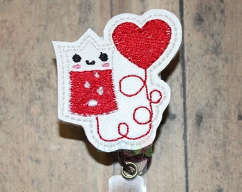 May include: White felt cartoon character holding a red heart balloon. The character has a red heart on its chest and a happy face. The character is attached to a clear plastic badge holder with a silver clip.