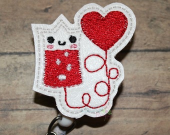 May include: White embroidered badge with a red heart balloon and a red and white cartoon character with a happy face. The badge has a white clip on the back.