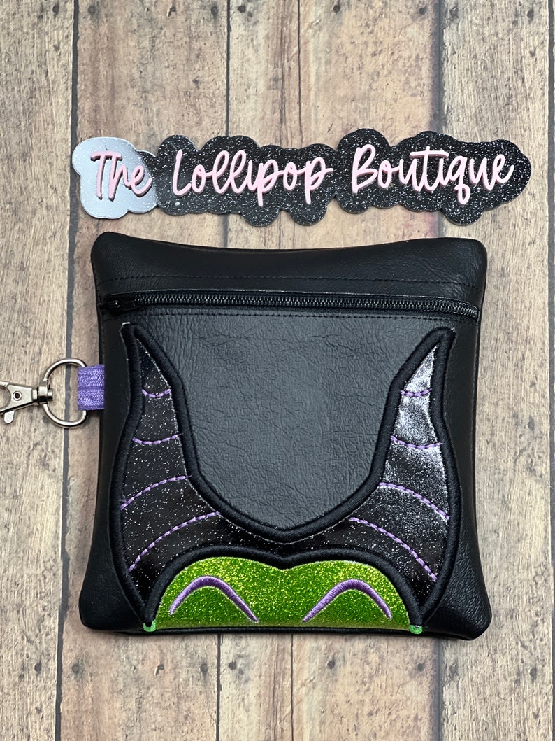 May include: Black zippered pouch with a glittery green and purple Maleficent design. The pouch has a zipper closure and a silver key chain.