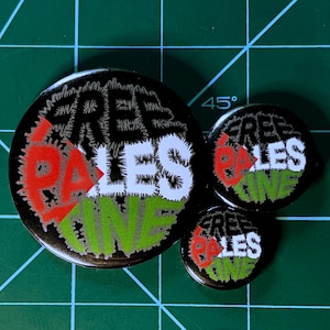 May include: Three black button pins with the text "Free Palestine" in white, green, and red lettering. The pins are different sizes.