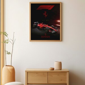 Puede incluir: Un p&oacute;ster enmarcado con un coche de carreras de F&oacute;rmula 1 rojo con el logotipo de Ferrari y el texto "SF-23". El coche est&aacute; sobre un fondo negro con luces rojas y blancas.