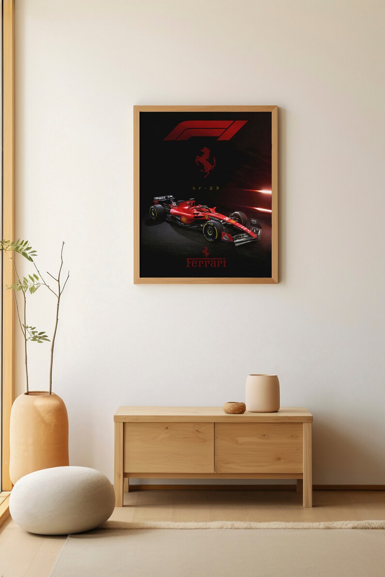 Puede incluir: Un p&oacute;ster enmarcado con un coche de carreras de F&oacute;rmula 1 rojo con el logotipo de Ferrari y el texto "SF-23". El coche est&aacute; sobre un fondo negro con luces rojas y blancas.