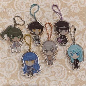 Puede incluir: Llaveros de acrílico con diseños de personajes de estilo anime. Cada llavero presenta un personaje diferente con colores de cabello y atuendos únicos. Los amuletos están unidos a cadenas de bolas metálicas de varios colores.