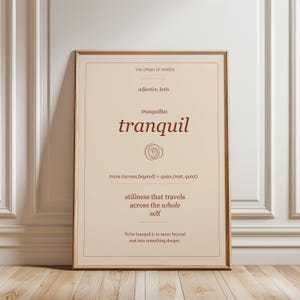 May include: A framed print featuring the word "tranquil" in a decorative font. The print provides the definition, origin, and related terms of the word. The colour scheme is neutral, with a beige background and brown text.