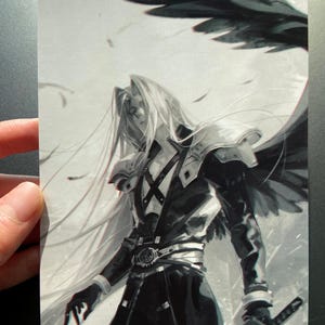 May include: Black and white illustration of a character with long silver hair, wearing a black coat and armor, holding a sword. The character has a wing-like structure behind them, with feathers floating in the air. The image is held by a hand.