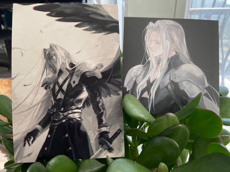 May include: Two art prints featuring a character with long silver hair and armor. One print shows the character with a wing and a sword, the other shows the character in profile. The prints are set against a black and white background.