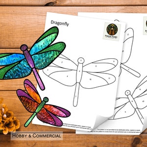 Pode incluir: Imagem de um padrão de vitral de libélula com um design colorido. A libélula é retratada em tons de azul, verde, roxo e laranja. A imagem também inclui um desenho linear do padrão da libélula e o texto "Dragonfly".