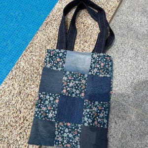 Può includere: Una borsa tote in denim blu con quadrati di patchwork in diverse tonalità di denim blu e tessuto floreale. La borsa ha due manici in denim nero.