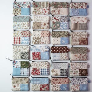 Può includere: Una collezione di piccole pochette rettangolari con cerniera patchwork. Ogni pochette presenta una combinazione unica di motivi floreali, a pois e a righe in vari colori, tra cui rosso, blu e beige. Le pochette hanno tiretti neri.