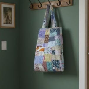 Könnte beinhalten: Eine Patchwork-Tragetasche mit einer Vielzahl von Stoffquadraten in Blau-, Grün-, Gelb- und Orangetönen. Die Tasche hängt an einer Holzstange an einer grünen Wand. Die Tasche hat zwei lange Träger.