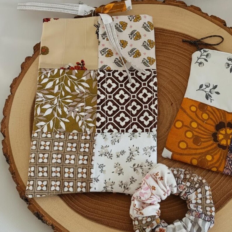 Op de afbeelding: Een verzameling stoffen items met diverse patronen, waaronder een patchwork tas, een klein zakje en een scrunchie. De tas heeft een mix van bloemen- en geometrische ontwerpen in beige, bruine en groene tinten. De items zijn gerangschikt op een houten oppervlak.