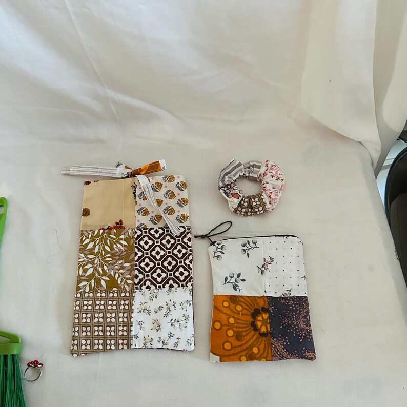 Op de afbeelding: Een verzameling handgemaakte stoffen accessoires, waaronder een patchwork etui, een kleine etui met ritssluiting en een scrunchie. De items hebben verschillende patronen in bruin-, beige- en wittinten, met bloemen- en geometrische ontwerpen.