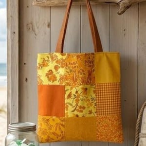 Pode incluir: Uma sacola tote de patchwork com uma variedade de padrões florais e geométricos laranja e amarelos. A sacola tem alças de couro marrom e está pendurada em uma parede de madeira. A sacola é de tamanho médio.