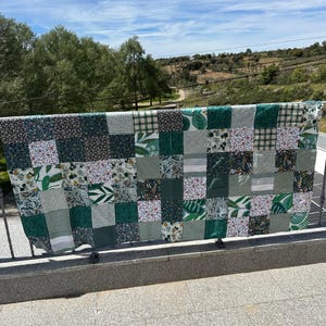 Pode incluir: Uma colcha de retalhos retangular composta por uma grade de quadrados de tecido em vários tons de verde, branco e preto. Os padrões incluem estampas de folhas botânicas, pequenos motivos florais, listras finas e texturas verde sólido.