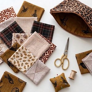 Pode incluir: Uma coleção de quadrados de tecido dobrados com vários padrões, incluindo estampa de leopardo, xadrez, listras e motivos de pássaros, junto com uma bolsa com zíper de leopardo, tesoura dourada, um carretel de madeira e uma almofada de alfinetes.