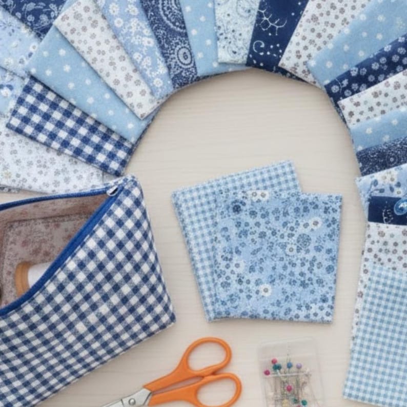 Pode incluir: Uma variedade de quadrados de tecido azul e branco com estampas florais, de bolinhas e paisley. Uma bolsa com z&iacute;per combinando, tesouras laranja e alfinetes tamb&eacute;m s&atilde;o vis&iacute;veis. Ideal para projetos de costura e patchwork.