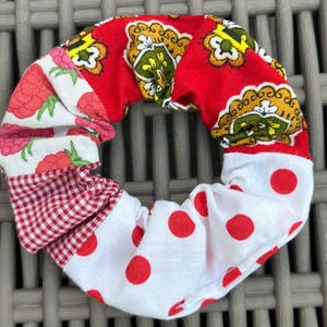 Puede incluir: Una colorida scrunchie con varios estampados de tela. Presenta lunares rojos y blancos, cuadros vichy rojos y blancos y diseños florales y paisley en rojo, amarillo y verde. Es un accesorio para el cabello.