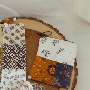 Op de afbeelding: Een patchwork etui en bladwijzer set. De etui heeft bloemen- en geometrische patronen in wit, oranje en marineblauw. De bladwijzer heeft vergelijkbare patronen in bruin, wit en beige.