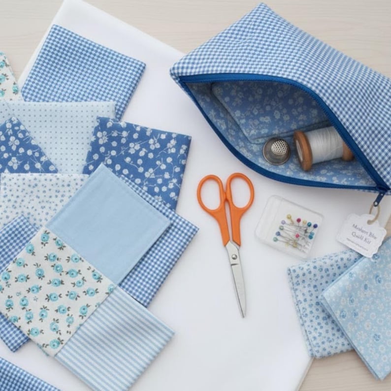 Pode incluir: Uma bolsa com z&iacute;per xadrez azul e branco com interior azul, revelando uma bobina de linha branca, uma dedeira e tesouras. V&aacute;rios quadrados de tecido azul com desenhos florais e estampados s&atilde;o dispostos ao redor da bolsa, junto com um pequeno recipiente de alfinetes.