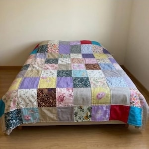 Könnte beinhalten: Eine Patchwork-Decke bestehend aus einem Raster aus quadratischen Stoffstücken in verschiedenen Farben und Mustern, darunter florale, gestreifte und einfarbige Designs in Rot, Blau, Gelb, Lila, Grün und Weiß, die die Oberfläche eines Bettes bedeckt.
