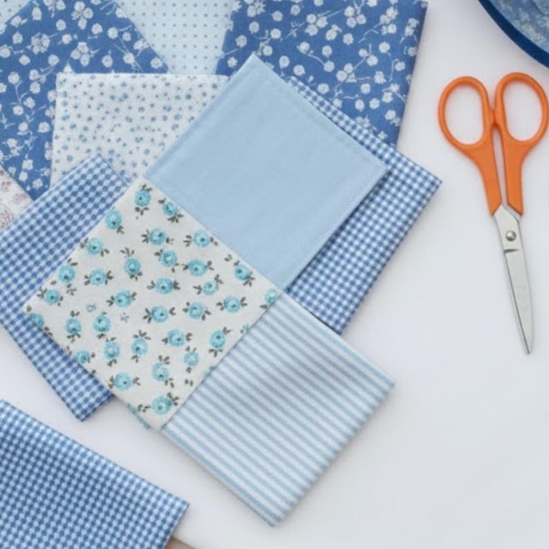 Pode incluir: Variedade de quadrados de tecido azul com v&aacute;rios padr&otilde;es, incluindo florais, xadrez e listras. Um par de tesouras com cabo laranja repousa sobre uma superf&iacute;cie branca, sugerindo um projeto de artesanato ou costura. Os tecidos s&atilde;o em tons de azul claro e m&eacute;dio.