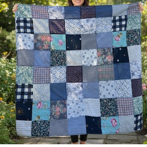 May include: A patchwork quilt in various shades of blue, with floral, checked, and plain fabric squares. The quilt is constructed from numerous squares stitched together, forming a textured design. The quilt is displayed against a natural backdrop.