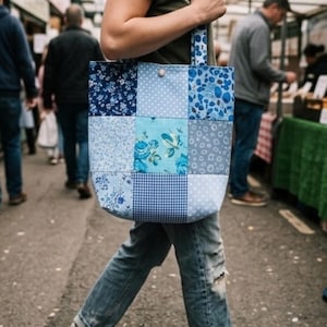 May include: A patchwork tote bag with a variety of blue patterns, including floral, polka dot, and gingham. The bag is carried by a person walking on a street.