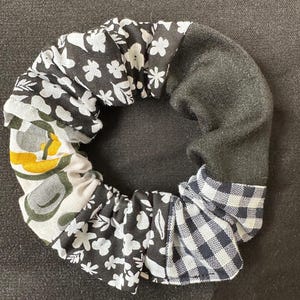 Könnte beinhalten: Ein Stoff-Haargummi mit einer Vielzahl von Mustern. Das Haargummi hat Abschnitte mit schwarz-weißem Blumendruck, einen einfarbigen schwarzen Abschnitt und einen Abschnitt mit schwarz-weißem Vichy-Karo. Das Haargummi ist zum Halten der Haare bestimmt.