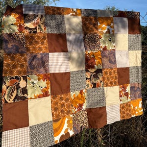 Könnte beinhalten: Eine Patchwork-Decke mit verschiedenen braunen, beige und orangefarbenen Blumenmustern. Die Decke besteht aus Quadraten aus verschiedenen Stoffen, die jeweils ein einzigartiges Design haben.