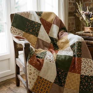May include: A patchwork quilt featuring a variety of square fabric blocks in shades of forest green, mustard yellow, cream, and terracotta. The quilt displays a mix of floral patterns, small-scale geometric prints, and a classic gingham check design.