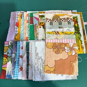 May include: A collection of colorful fabric scraps, featuring various patterns and designs. The fabrics include floral prints, stripes, and geometric shapes in shades of pink, yellow, green, and orange. The pieces are arranged on a green cutting mat.