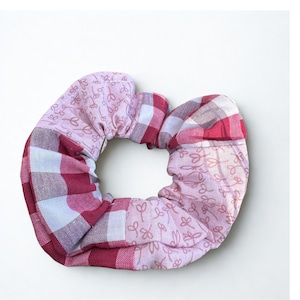 Könnte beinhalten: Ein handgefertigtes Scrunchie mit Patchwork-Design. Das Scrunchie hat eine Mischung aus rosa und roten Stoffen, darunter ein Vichy-Muster und ein Blumendruck. Das Scrunchie ist dafür konzipiert, das Haar in einem Pferdeschwanz oder Dutt zu halten.