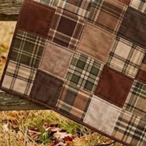May include: A patchwork quilt featuring a repeating grid of square fabric panels. The design alternates between solid dark brown squares and plaid patterned squares in shades of forest green, tan, beige, and dark brown with visible stitching.
