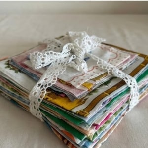Pode incluir: Uma pilha de lenços vintage coloridos amarrados com uma fita de renda branca. Os lenços apresentam vários padrões e cores, incluindo florais, bolinhas e designs geométricos. A fita de renda adiciona um toque delicado ao conjunto.