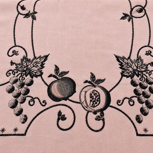May include: A light pink fabric featuring black machine embroidery. The design includes two clusters of grapes with leaves, a whole pomegranate, and a halved pomegranate. The motifs are connected by scrolling vines and framed by a border with stars.