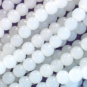 May include: A strand of white round beads made of polished white agate. The beads are smooth and have a slightly translucent appearance.