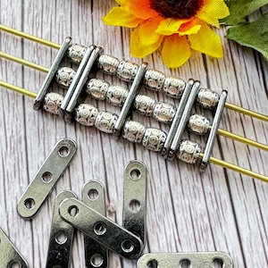 May include: A set of silver metal beads with a geometric pattern, arranged in a ladder-like formation. The beads are strung on three gold wires. There are also several silver metal connector pieces with four holes each.