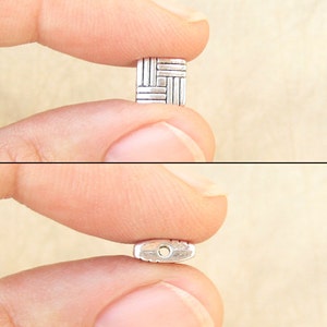 8 millimeter puff square beads with a basketweave design with fingers for scale