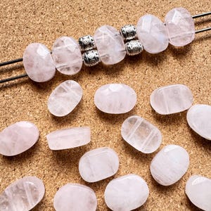 May include: Rose quartz gemstone beads in various shapes and sizes. Some beads are strung on a wire, while others are loose. The beads are a soft pink color and have a translucent quality. Silver-colored metal beads are also present.
