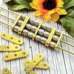May include: A set of gold-toned metal bracelet components with silver-toned beads. The beads have a decorative pattern. The components are arranged on a wooden surface with a sunflower.