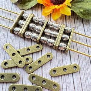 May include: A set of 10 antique gold-toned metal connector pieces with four holes each. The connector pieces are rectangular and have a slightly textured surface. The connector pieces are arranged on a wooden surface.