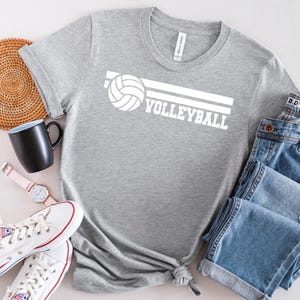 Op de afbeelding: Grijs T-shirt met een witte volleybalafbeelding en het woord "VOLLEYBALL" erop gedrukt.