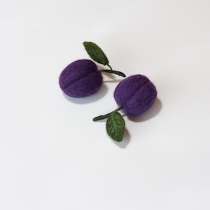 May include: Two purple felt plums with green felt leaves. The plums are round and have a slightly textured surface.