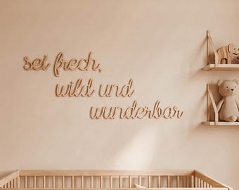 May include: Wooden wall decor with the German phrase "sei frech, wild und wunderbar" in a cursive font. The nursery scene includes a wooden crib, shelves with toys, and a neutral color palette.