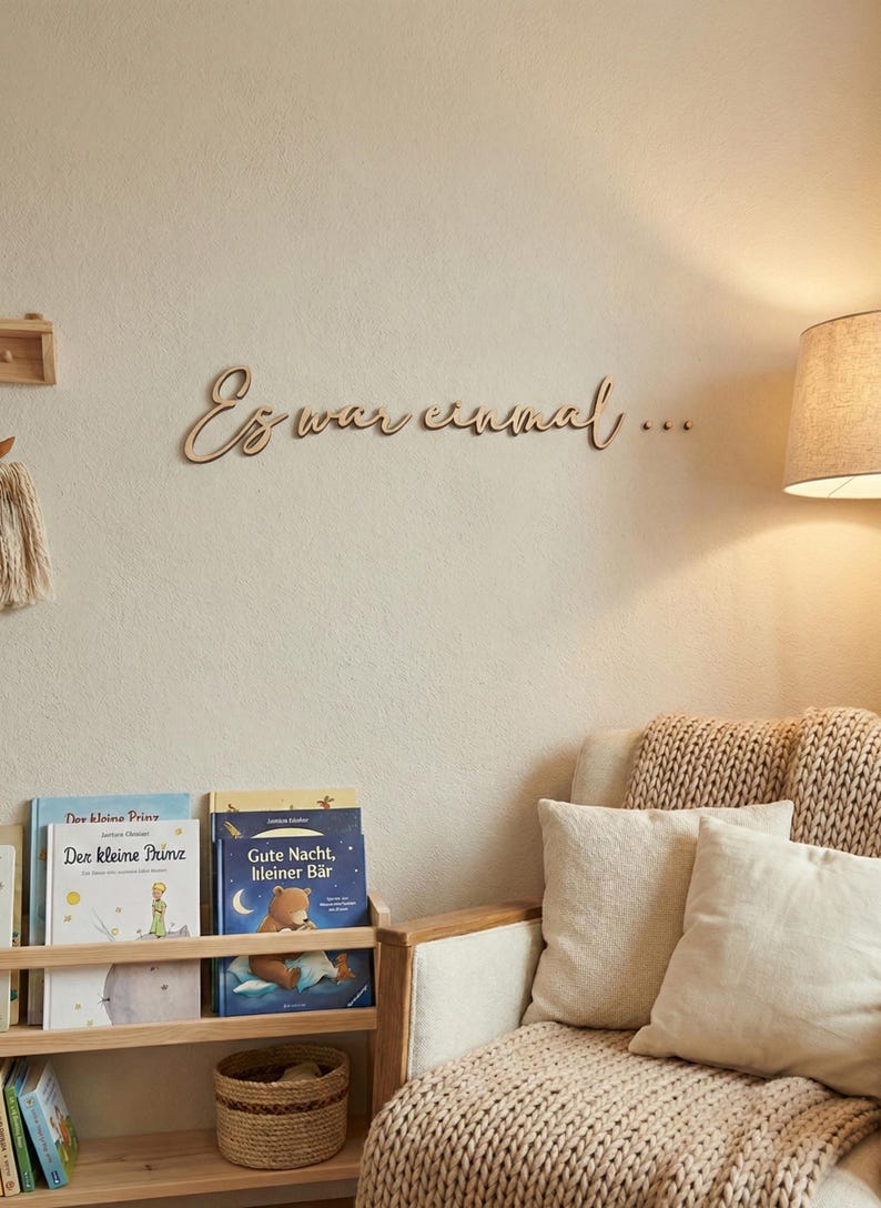 May include: Wooden wall decor with the phrase "Es war einmal..." in cursive script. The room features a bookshelf with children's books, a cozy armchair with pillows, and a woven blanket. A lamp provides soft lighting.
