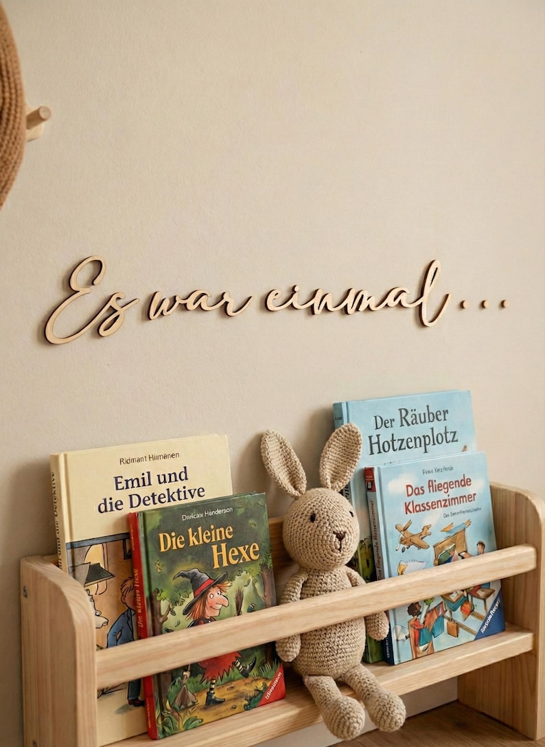 May include: Wooden bookshelf with children's books and a crocheted bunny. The books include "Emil und die Detektive", "Die kleine Hexe", "Der R&auml;uber Hotzenplotz", and "Das fliegende Klassenzimmer". Above the shelf is wooden text that reads "Es war einmal..."