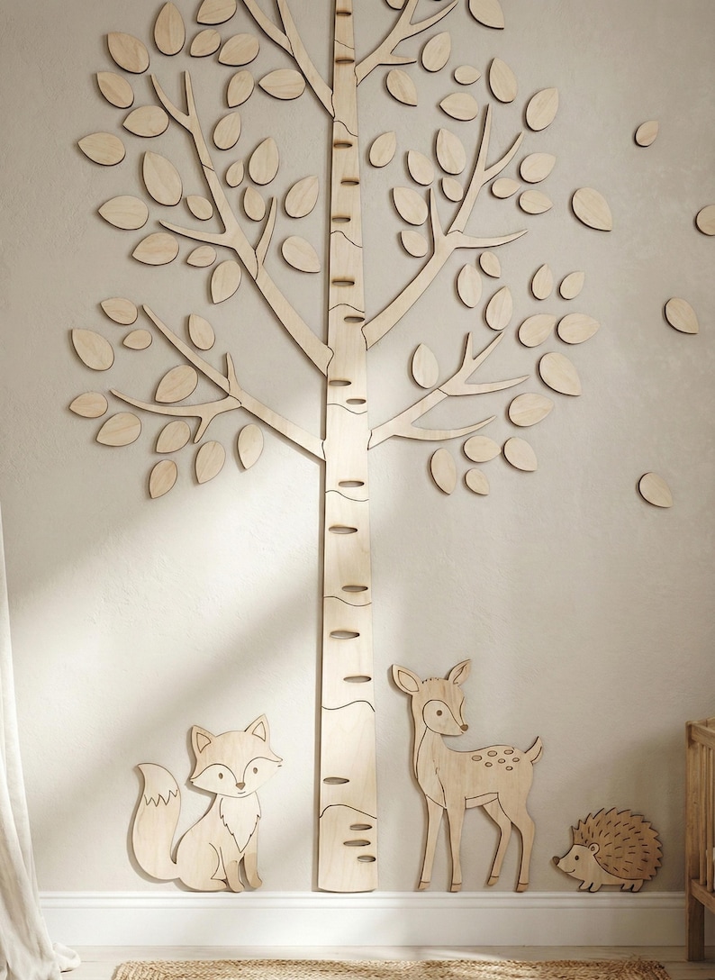 May include: Wooden wall decor featuring a birch tree with leaves, a fox, a deer, and a hedgehog. The tree trunk has measurement markings. The light-colored wood pieces are mounted on a neutral-toned wall, creating a woodland theme.
