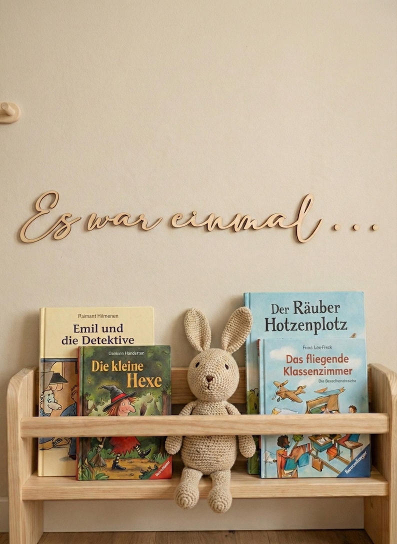May include: A wooden bookshelf with children's books and a stuffed bunny. The books include titles like "Emil and the Detectives" and "The Little Witch." Above the shelf, the phrase "Es war einmal..." is displayed.