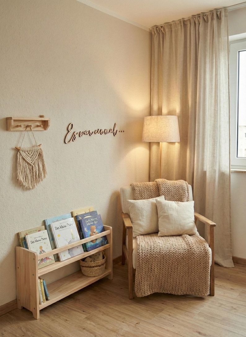 May include: A cozy reading nook with a wooden bookshelf filled with books, a macrame wall hanging, and a wooden chair with pillows and a knitted throw. The wall features the text "Es war einmal..." in cursive.