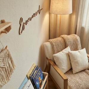 May include: A cozy reading nook with a wooden floor lamp and a beige armchair. The wall features a wooden sign that says "Erwasund..." and a small wooden shelf. A wooden bookshelf holds several children's books.